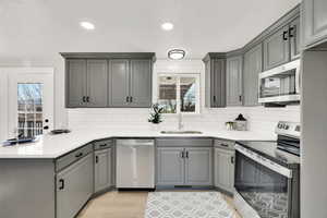 Kitchen with gray cabinets, sink, light wood-type flooring, and stainless steel appliances