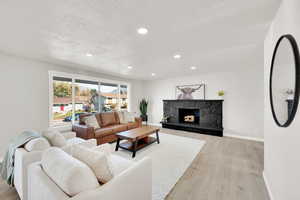 Living room featuring a textured ceiling, light wood-type flooring, and a stone fireplace