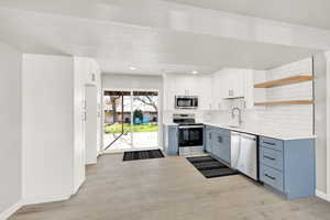 Kitchen featuring backsplash, white cabinets, sink, light hardwood / wood-style flooring, and appliances with stainless steel finishes