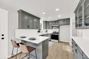 Kitchen with gray cabinetry, sink, a kitchen breakfast bar, light hardwood / wood-style flooring, and appliances with stainless steel finishes