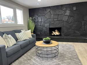 Living room with a stone fireplace, wood-type flooring, and a textured ceiling