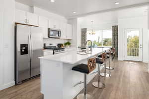 Kitchen with white cabinets, stainless steel appliances, a kitchen island with sink, and light hardwood / wood-style floors