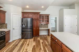 Kitchen with light wood-type flooring, stainless steel refrigerator with ice dispenser, and backsplash