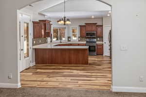 Kitchen with backsplash, kitchen peninsula, a notable chandelier, wood-type flooring, and stainless steel appliances