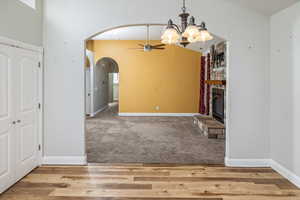 Unfurnished dining area featuring a fireplace, light hardwood / wood-style flooring, and ceiling fan with notable chandelier