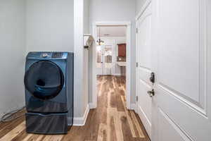 Clothes washing area featuring washer / dryer, an inviting chandelier, and light hardwood / wood-style flooring