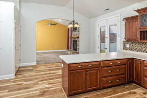 Kitchen featuring lofted ceiling, ceiling fan with notable chandelier, light wood-type flooring, a fireplace, and kitchen peninsula