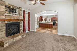 Unfurnished living room with a fireplace, ceiling fan with notable chandelier, light colored carpet, and lofted ceiling