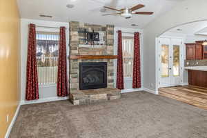 Unfurnished living room featuring carpet flooring, a stone fireplace, and ceiling fan