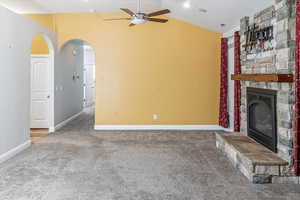 Unfurnished living room featuring ceiling fan, a fireplace, carpet, and vaulted ceiling