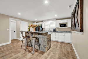 Kitchen featuring light stone counters, light hardwood / wood-style flooring, a center island, white cabinetry, and a breakfast bar area