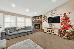 Living room featuring carpet floors, vaulted ceiling, and a stone fireplace