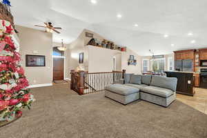 Carpeted living room featuring ceiling fan with notable chandelier and high vaulted ceiling