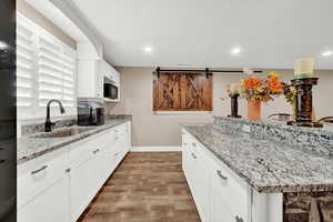 Kitchen featuring white cabinetry, sink, light stone countertops, and hardwood / wood-style flooring