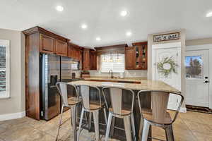 Kitchen featuring light stone counters, a center island, sink, and stainless steel refrigerator with ice dispenser