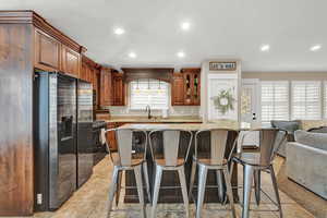 Kitchen with black gas range, sink, stainless steel fridge, a kitchen island, and a breakfast bar area