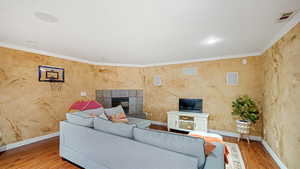 Living room with wood-type flooring, ornamental molding, and a tiled fireplace