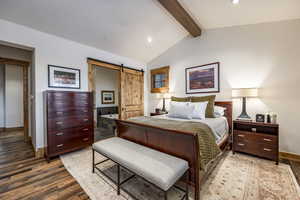 Bedroom featuring lofted ceiling with beams, a barn door, wood-type flooring, and ensuite bath