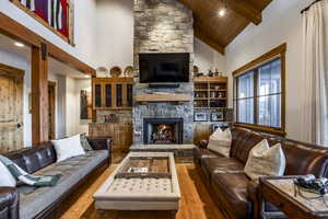 Living room with beam ceiling, hardwood / wood-style flooring, high vaulted ceiling, wooden ceiling, and a stone fireplace