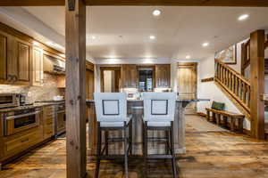 Kitchen with light stone countertops, a kitchen breakfast bar, tasteful backsplash, stainless steel appliances, and wood-type flooring