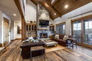 Living room featuring hardwood / wood-style flooring, high vaulted ceiling, wooden ceiling, and a stone fireplace