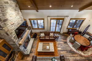 Living room with beam ceiling, a stone fireplace, wood ceiling, and dark hardwood / wood-style floors