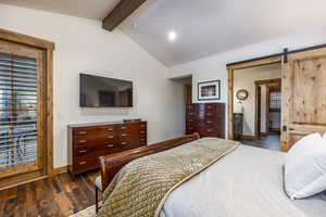 Bedroom featuring a barn door, ensuite bathroom, dark hardwood / wood-style flooring, and lofted ceiling with beams