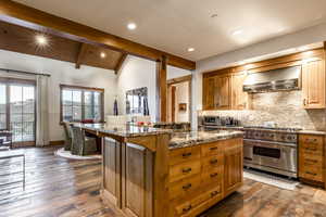 Kitchen featuring premium range, a breakfast bar, a center island, wall chimney range hood, and vaulted ceiling with beams