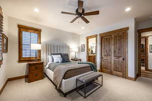 Bedroom with ensuite bathroom, ceiling fan, and light colored carpet