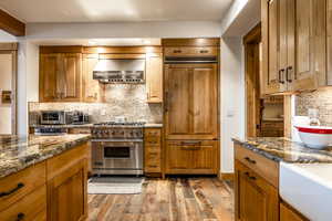 Kitchen with high quality appliances, dark wood-type flooring, wall chimney exhaust hood, decorative backsplash, and stone countertops