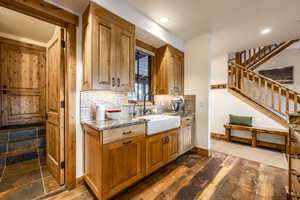 Kitchen with backsplash, stone countertops, sink, and dark wood-type flooring