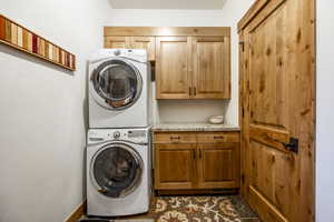 Washroom with cabinets, stacked washer and dryer, and dark tile patterned flooring