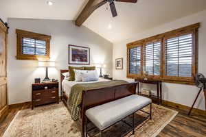 Bedroom featuring vaulted ceiling with beams, ceiling fan, dark wood-type flooring, and a barn door