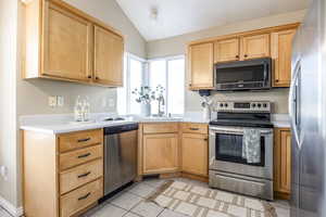 Kitchen featuring sink, vaulted ceiling, light brown cabinetry, light tile patterned floors, and appliances with stainless steel finishes