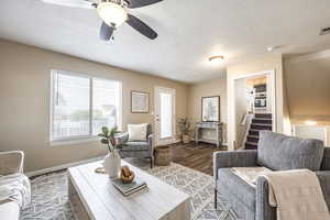 Living room with a textured ceiling, ceiling fan, and dark wood-type flooring