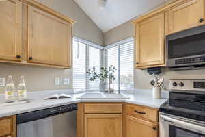 Kitchen featuring light brown cabinets, sink, lofted ceiling, and appliances with stainless steel finishes