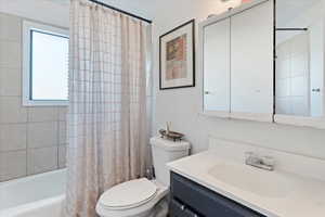 Full bathroom with vanity, shower / bathtub combination with curtain, and toilet