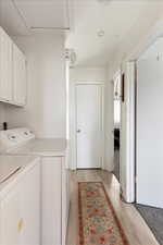 Laundry area featuring washing machine and clothes dryer, cabinets, and light wood-type flooring