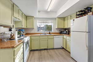 Kitchen with white appliances, light hardwood / wood-style flooring, green cabinets, and sink