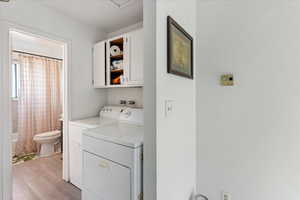 Laundry area with independent washer and dryer, cabinets, and light wood-type flooring