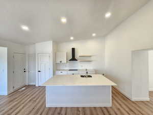 Kitchen with a kitchen island with sink, sink, white cabinets, lofted ceiling, and range hood