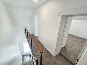 Corridor featuring vaulted ceiling and dark carpet