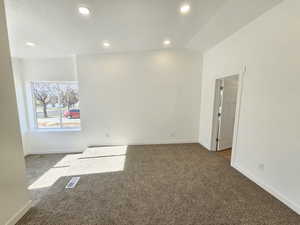 Unfurnished room with dark colored carpet, a textured ceiling, and vaulted ceiling