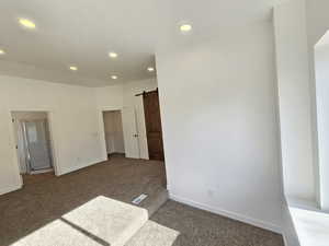 Unfurnished bedroom with a barn door and dark carpet