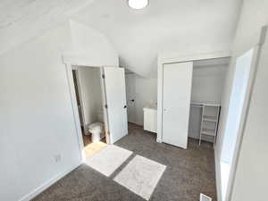 Unfurnished bedroom featuring carpet, ensuite bathroom, and lofted ceiling