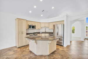 Kitchen with dark stone counters, sink, appliances with stainless steel finishes, a kitchen island, and a kitchen bar