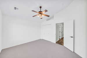 Carpeted spare room with ceiling fan and vaulted ceiling