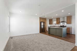 Kitchen featuring a wealth of natural light, a kitchen island, wall chimney range hood, and appliances with stainless steel finishes