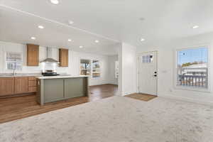 Kitchen featuring sink, wall chimney exhaust hood, light wood-type flooring, a kitchen island, and stainless steel range oven