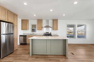 Kitchen featuring light hardwood / wood-style floors, a center island, wall chimney range hood, and stainless steel appliances